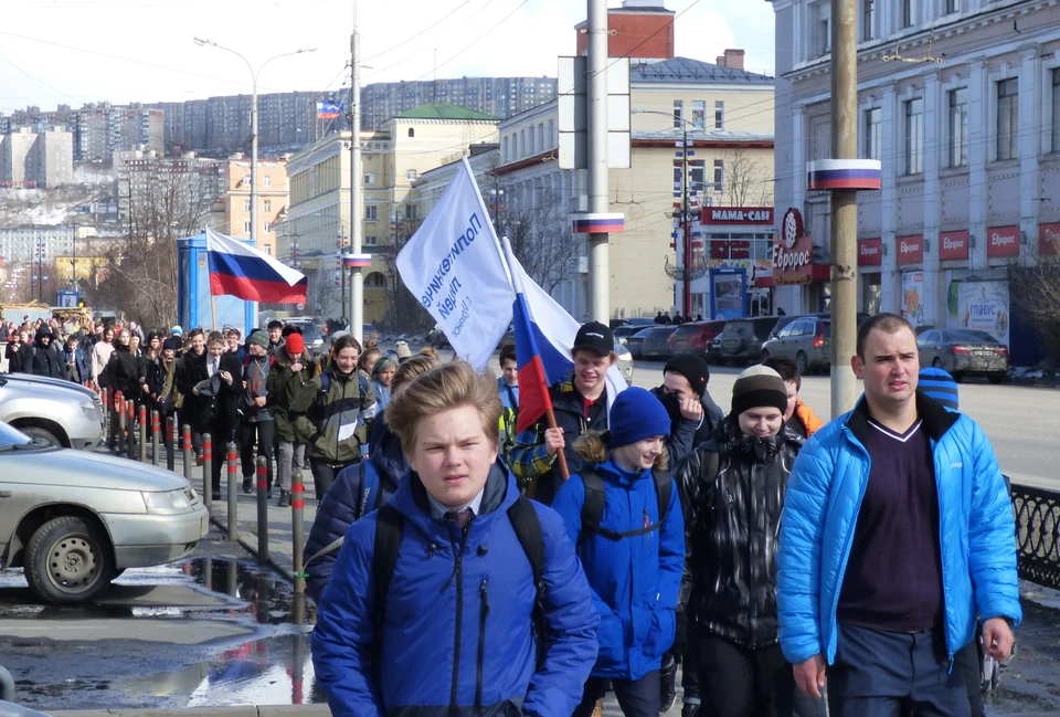 Школьники шагали на праздник, размахивая флагами.