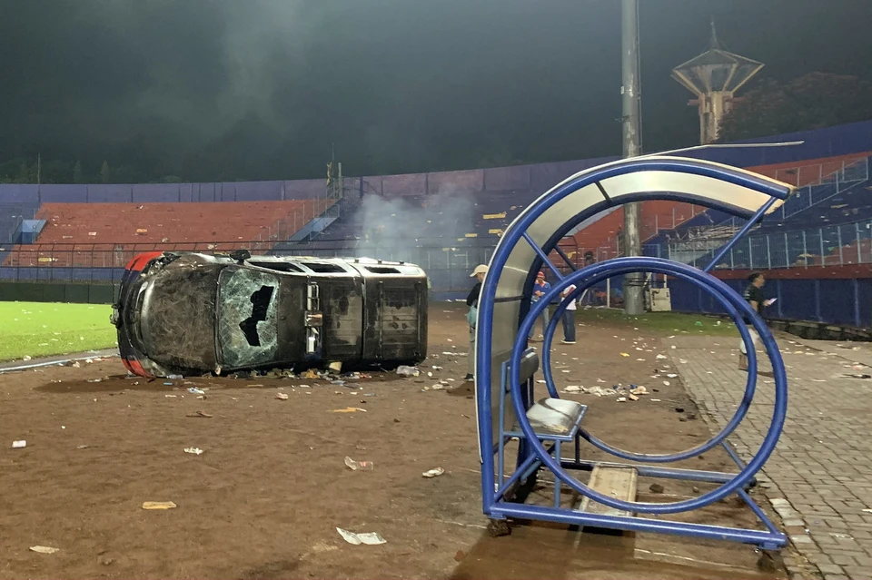 A wrecked police car and empty stadium stands in Indonesia, where a terrible tragedy happened.