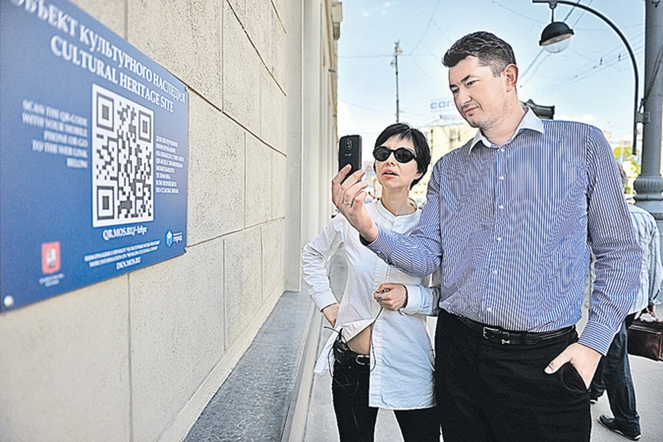 Мужчина и женщина считывают QR-код объекта культурного наследия с помощью мобильного телефона.