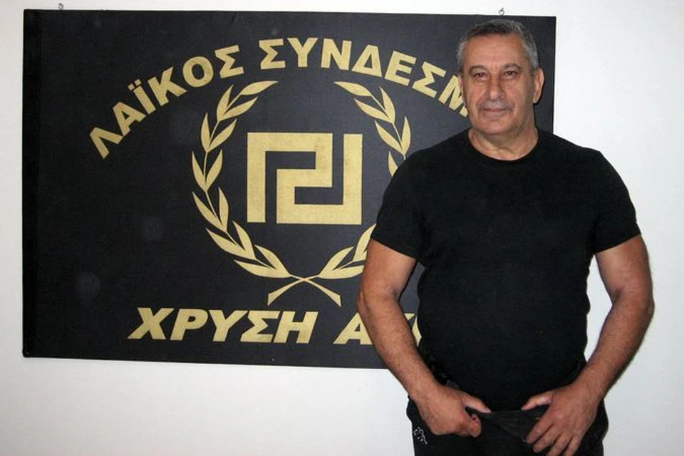Один из лидеров афинских националистов Янис Вулдис на фоне эмблемы своей партии - древнегреческой свастики.